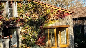 Une maison avec une façade en pierre, un porche en bois et une façade recouverte de vigne.