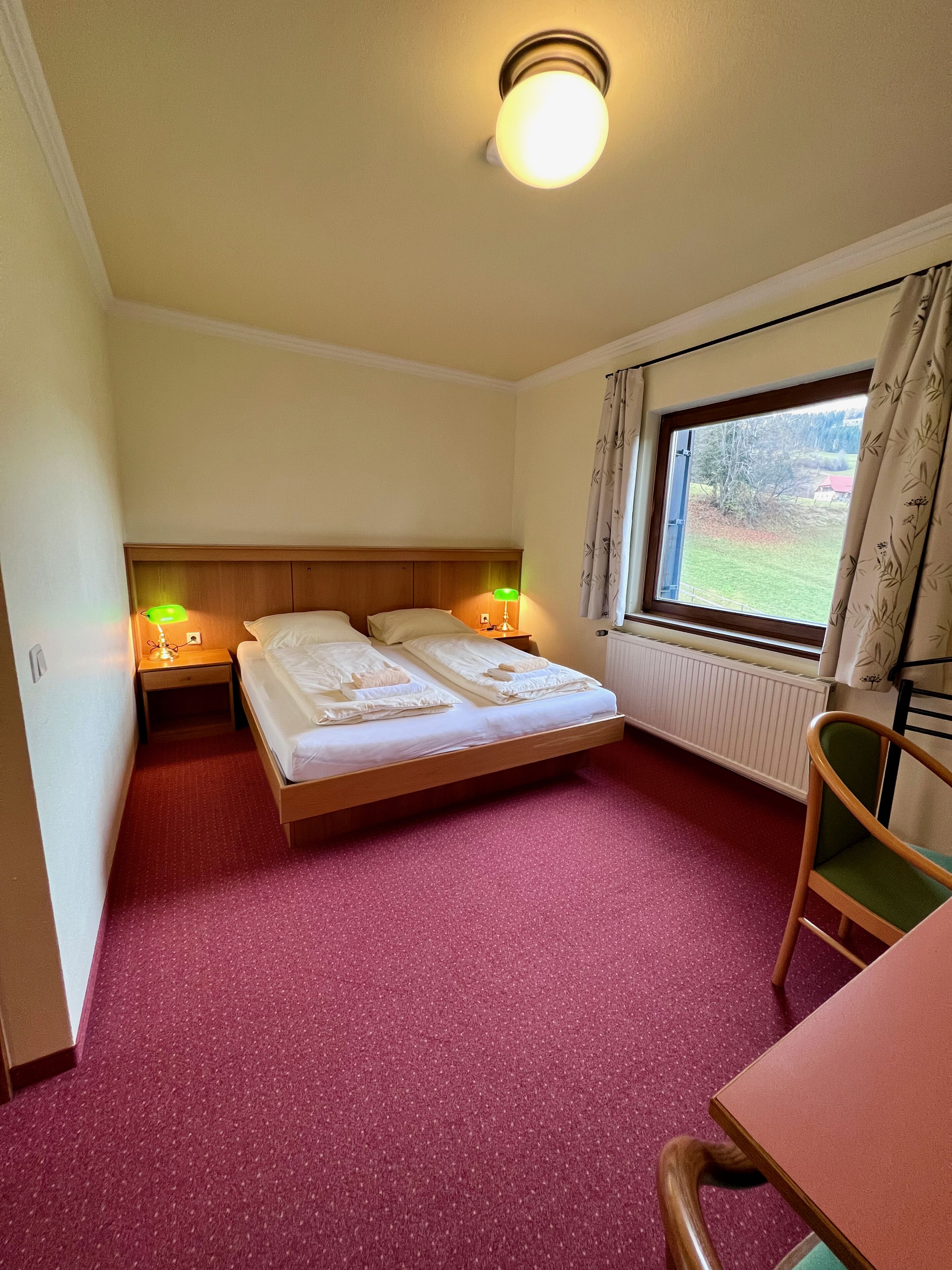 Un dormitorio con cama, dos mesitas de noche con lámparas, una ventana con cortinas y una silla.