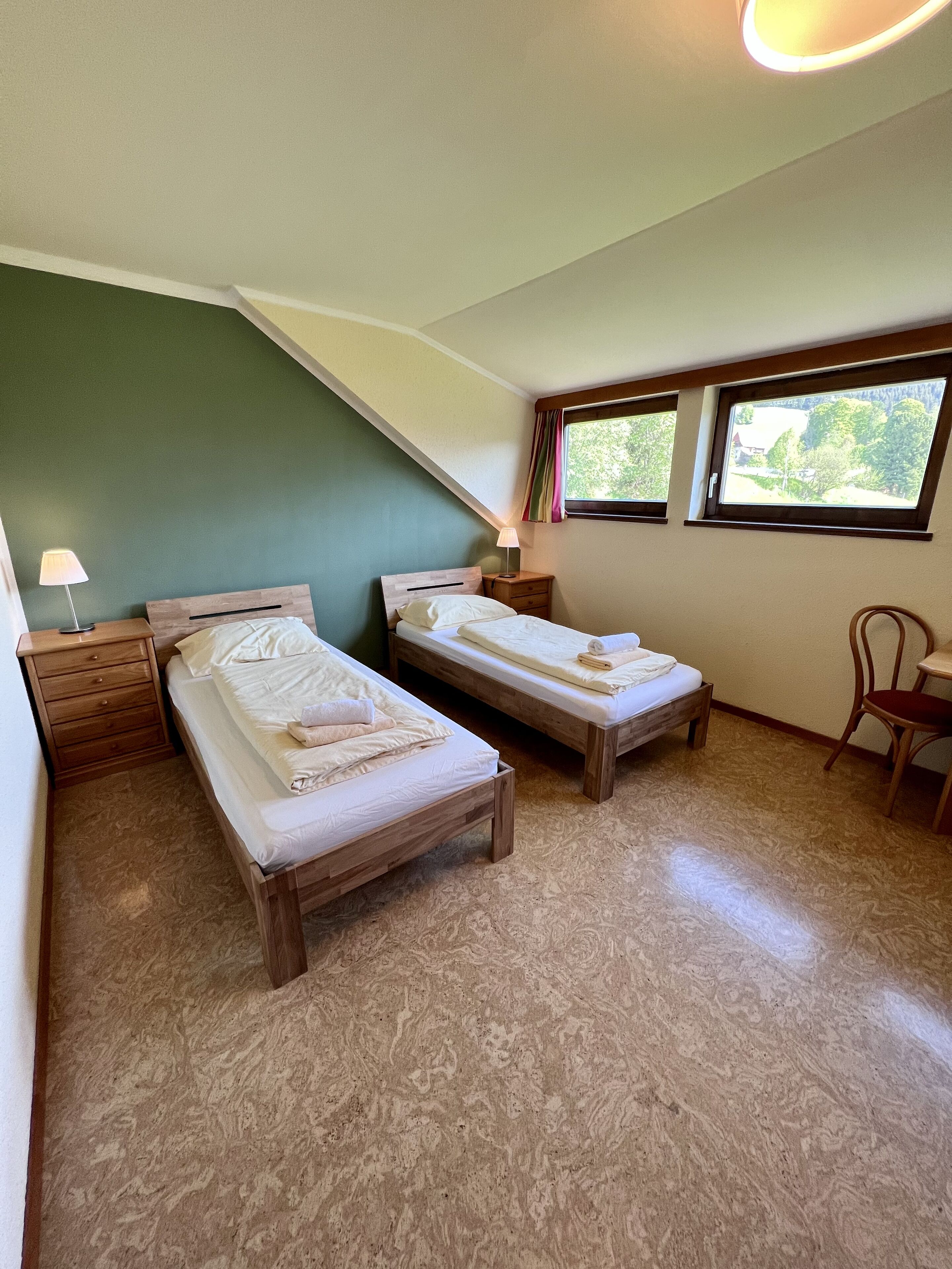A room with two wooden beds, a small wooden table, and a chair.