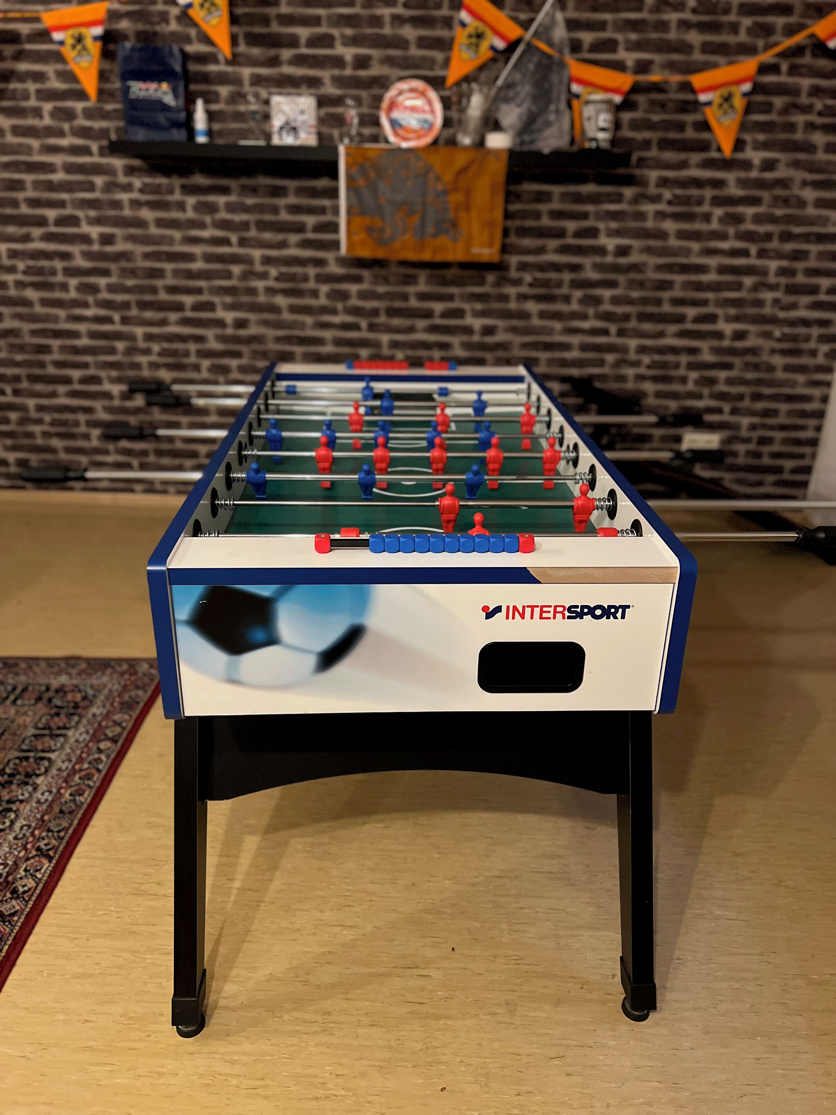 A foosball table with the INTERSPORT logo, set against a brick wall with banners.