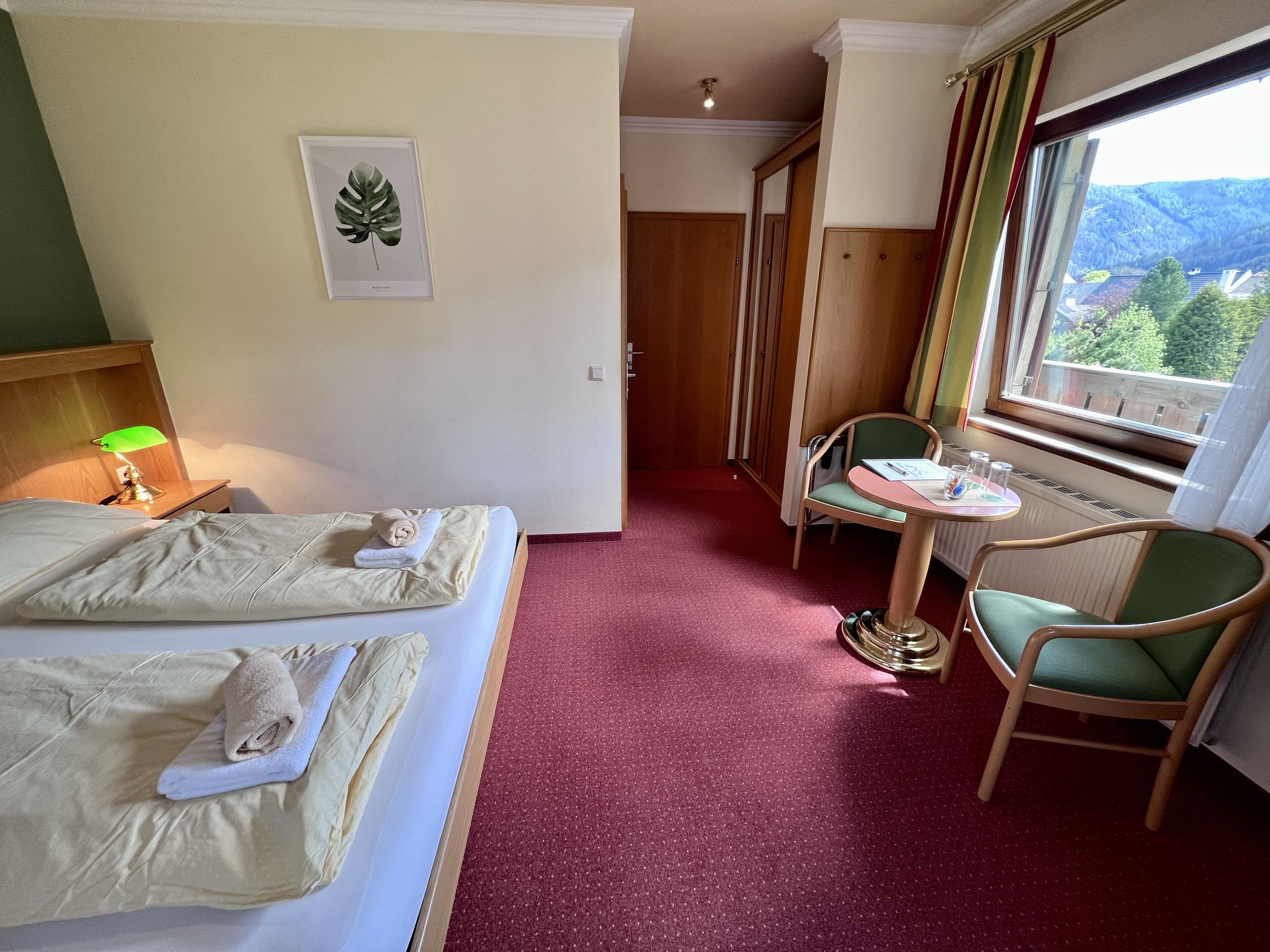 A hotel room with a bed, a desk, a chair, a small table, and a window with a view of mountains.