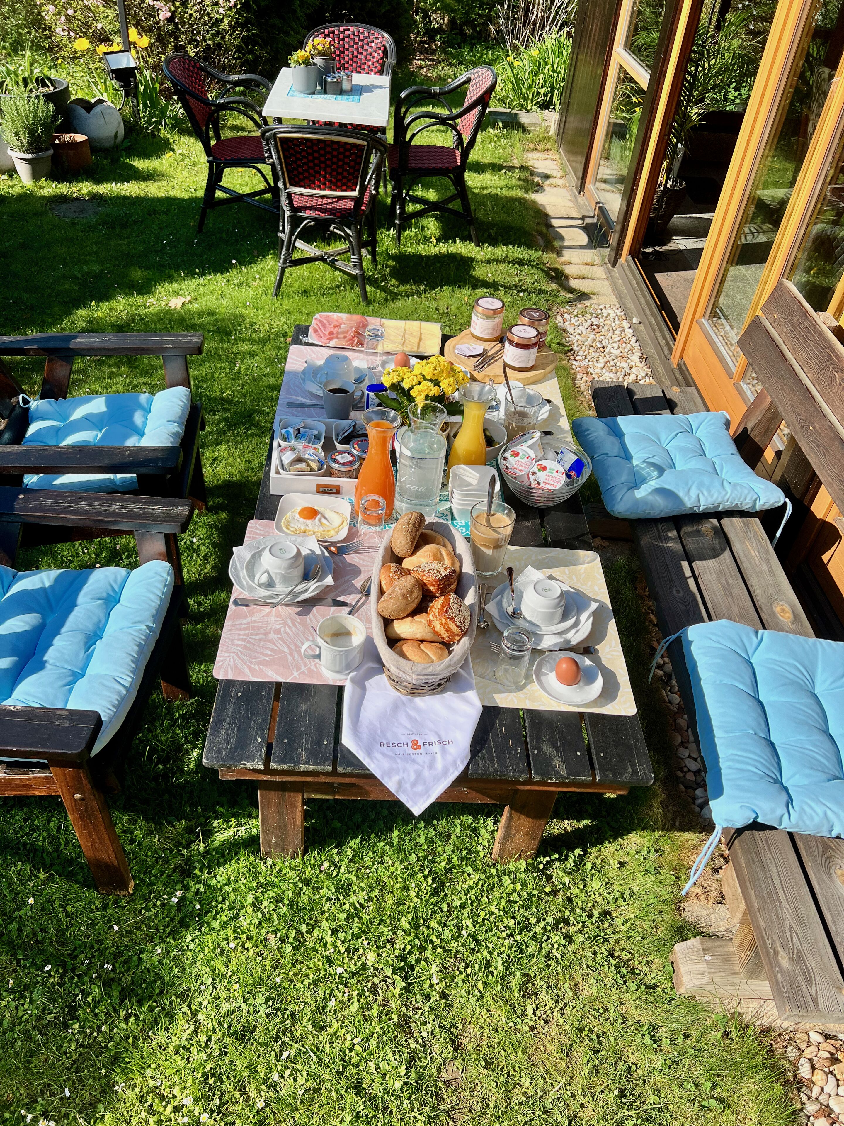 An outdoor breakfast setup with a table, chairs, and a variety of breakfast items.