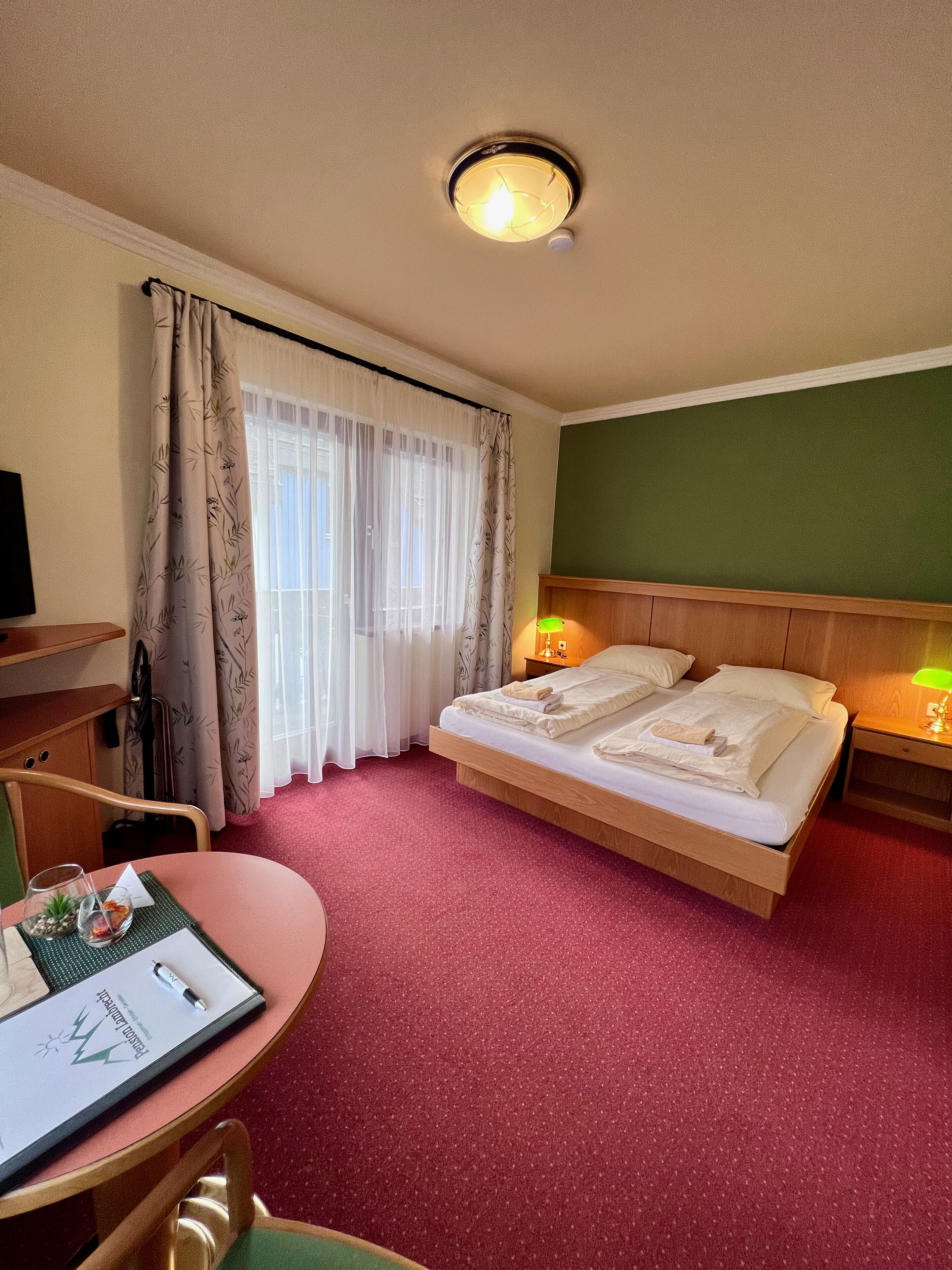 A hotel room with a bed, bedside lamps, a desk with a chair, and a window with curtains.