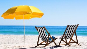 Two beach chairs with striped cushions and a yellow umbrella on a sandy beach with the ocean in the background. - LAKE/GOLF COURSE, screened porch~ Golf Cart~ FREE Activities~ Pool, HotTub (Miramar Beach)