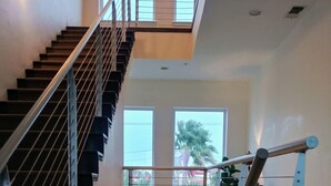 A modern interior with a staircase, a balcony, and a view of the outside. - Modern Family SPI Retreat- Waterfront, Wildlife, Sunrise & Sunset Views (South Padre Island)
