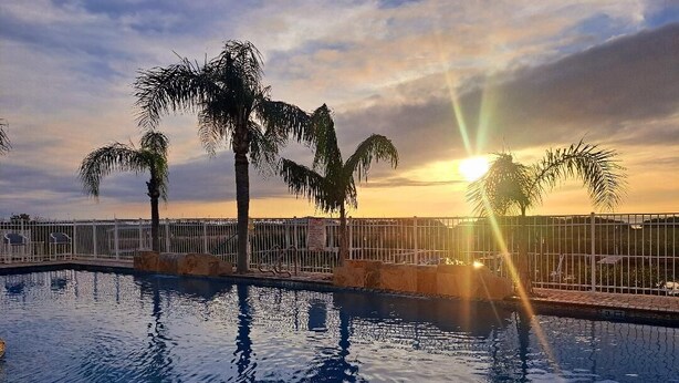 A swimming pool with palm trees and a sunset in the background. - Modern Family SPI Retreat- Waterfront, Wildlife, Sunrise & Sunset Views (South Padre Island)