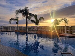 Une piscine bordée de palmiers, avec un coucher de soleil en arrière-plan.