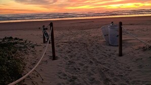 A beach with a rope barrier, a bicycle, and two large containers. - Modern Family SPI Retreat- Waterfront, Wildlife, Sunrise & Sunset Views (South Padre Island)