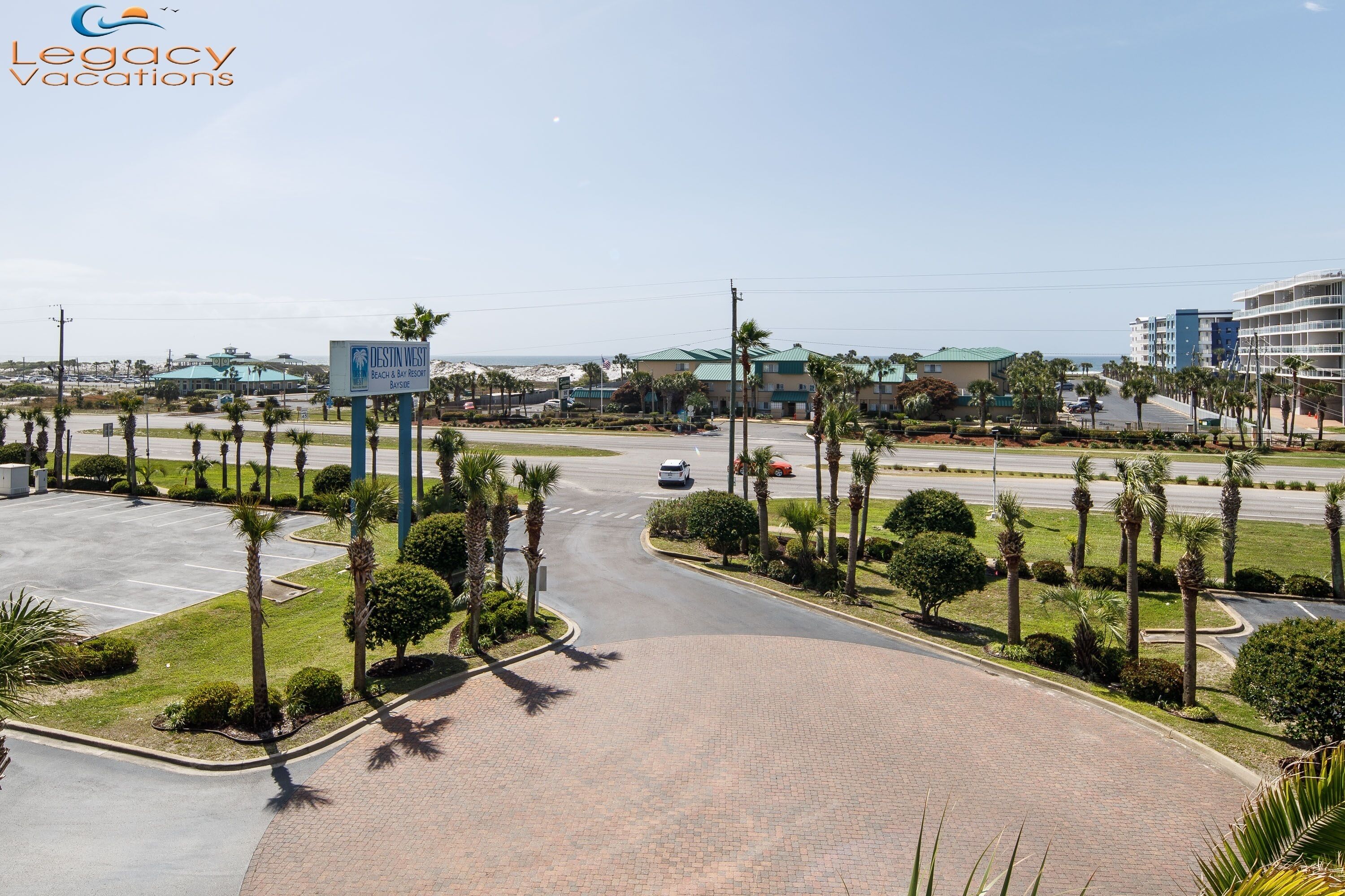 A view of Destiny West Beach Resort's parking area with palm trees and a clear sky.