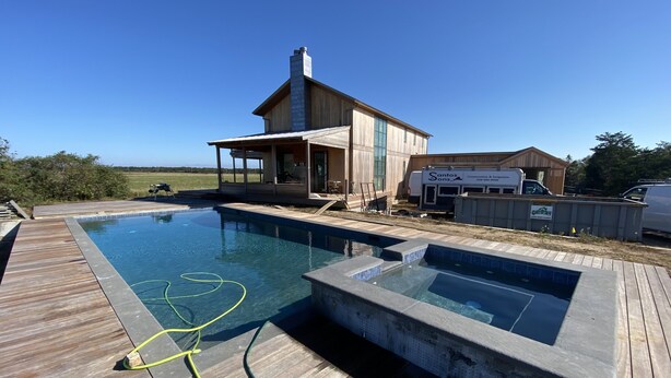 A modern house with a swimming pool and hot tub, surrounded by a wooden deck and a clear blue sky. - Up-island vibe, down-island conveniences. (Edgartown)