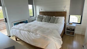 A bedroom with a large bed, a bedside table, a lamp, and a window with a view of greenery. - Up-island vibe, down-island conveniences. (Edgartown)