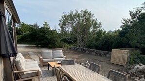 An outdoor deck with a wooden table and chairs, a sofa, and a covered seating area. - Up-island vibe, down-island conveniences. (Edgartown)