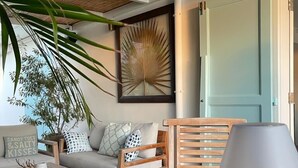 Una camera accogliente con soffitto in legno, un tavolino rotondo con lampada, un divano con cuscini e una pianta grande.