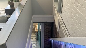 Eine Treppe mit weißer Geländer, einer Backsteinmauer und einer Holztür am unteren Ende.