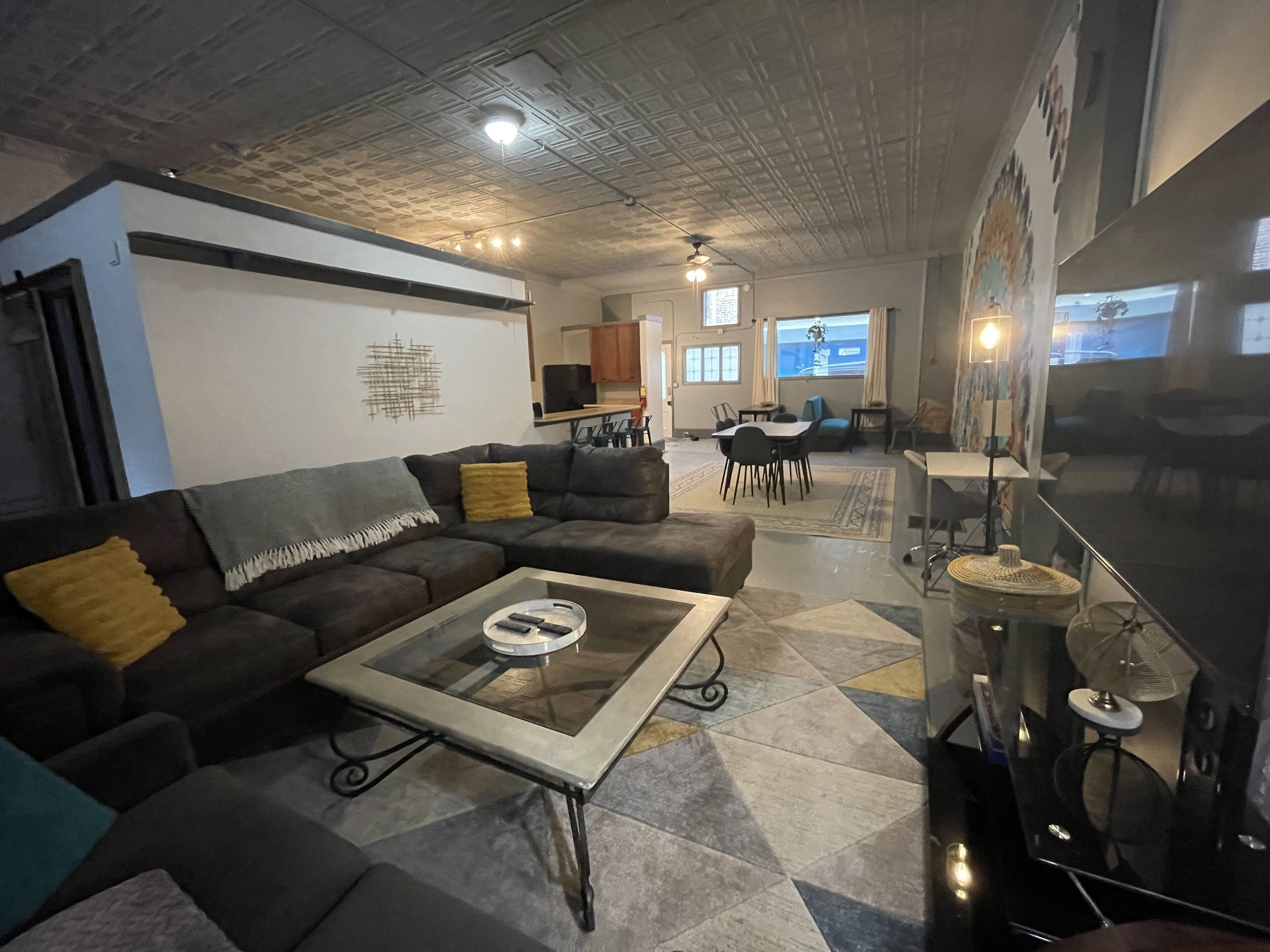 A modern living room with a sectional sofa, a glass coffee table, and a kitchen area in the background.