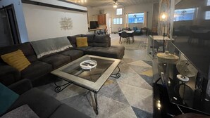 Ein modernes Wohnzimmer mit einem Ecksofa, einem Glastisch und einer Küche im Hintergrund.