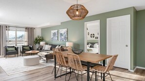 Una sala de estar moderna con comedor, que presenta una gran mesa de madera, sillas de mimbre, una mesa de centro redonda y una lámpara colgante.