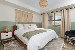 Camera da letto con un letto, un comodino, un pannello decorativo in macramè e una finestra con tende.
