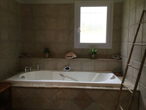 Un baño con bañera, una ventana y dos macetas en el alféizar.
