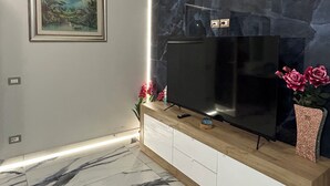 Una sala de estar moderna con piso de mármol, un televisor sobre un mueble de madera, un cuadro en la pared y un jarrón con flores.