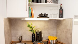 A compact kitchen with a sink, a coffee maker, a small refrigerator, and a countertop with a plant and some books.
