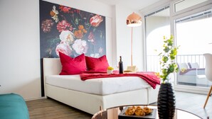 A modern living room with a white sofa, red pillows, a glass coffee table, and a large floral painting on the wall.