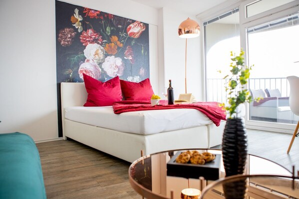 A modern living room with a white sofa, red pillows, a glass coffee table, and a large floral painting on the wall. - ☆Modern Apartment☆Panoramic View☆29th Floor☆Netflix☆Downtown☆ (Augsburg)