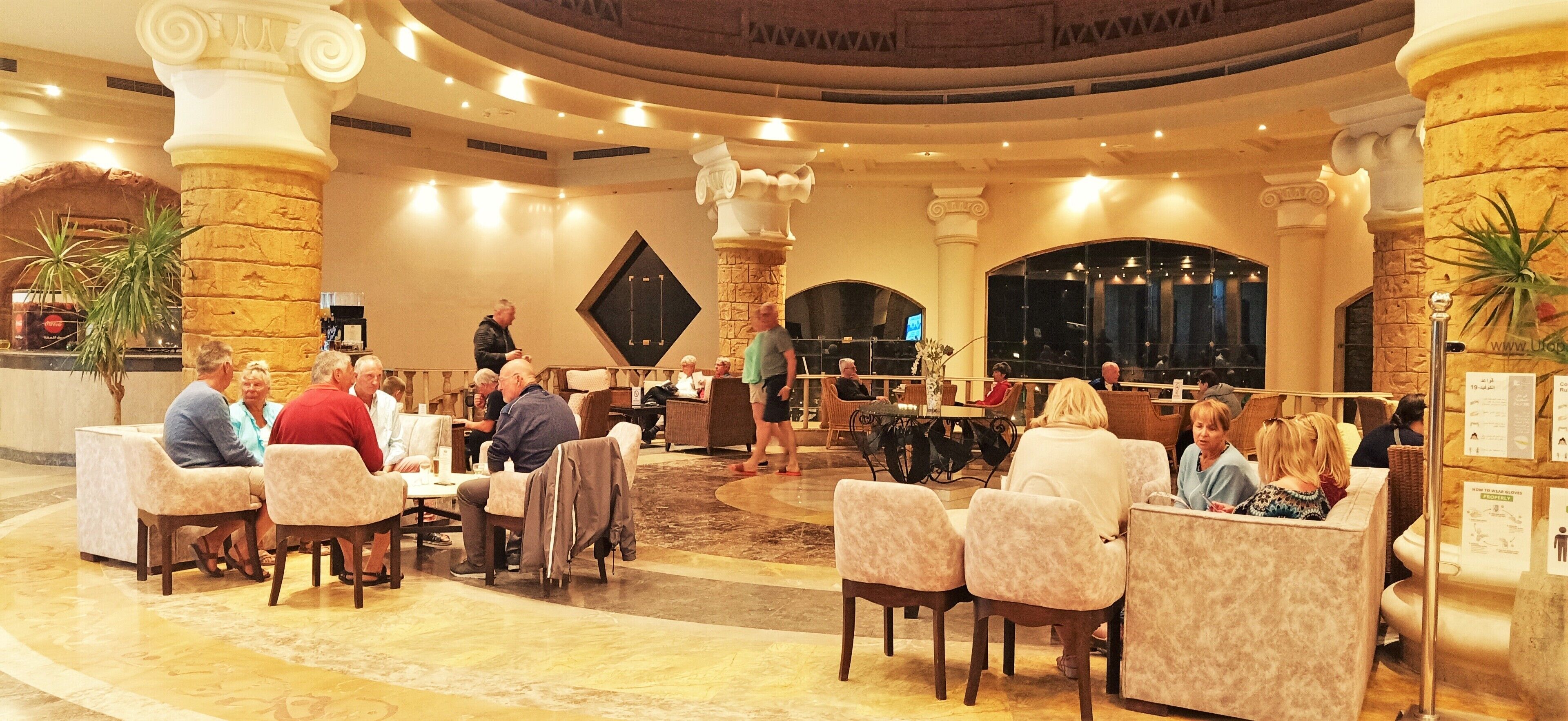 A spacious lobby with multiple seating areas, a central stage, and decorative columns.