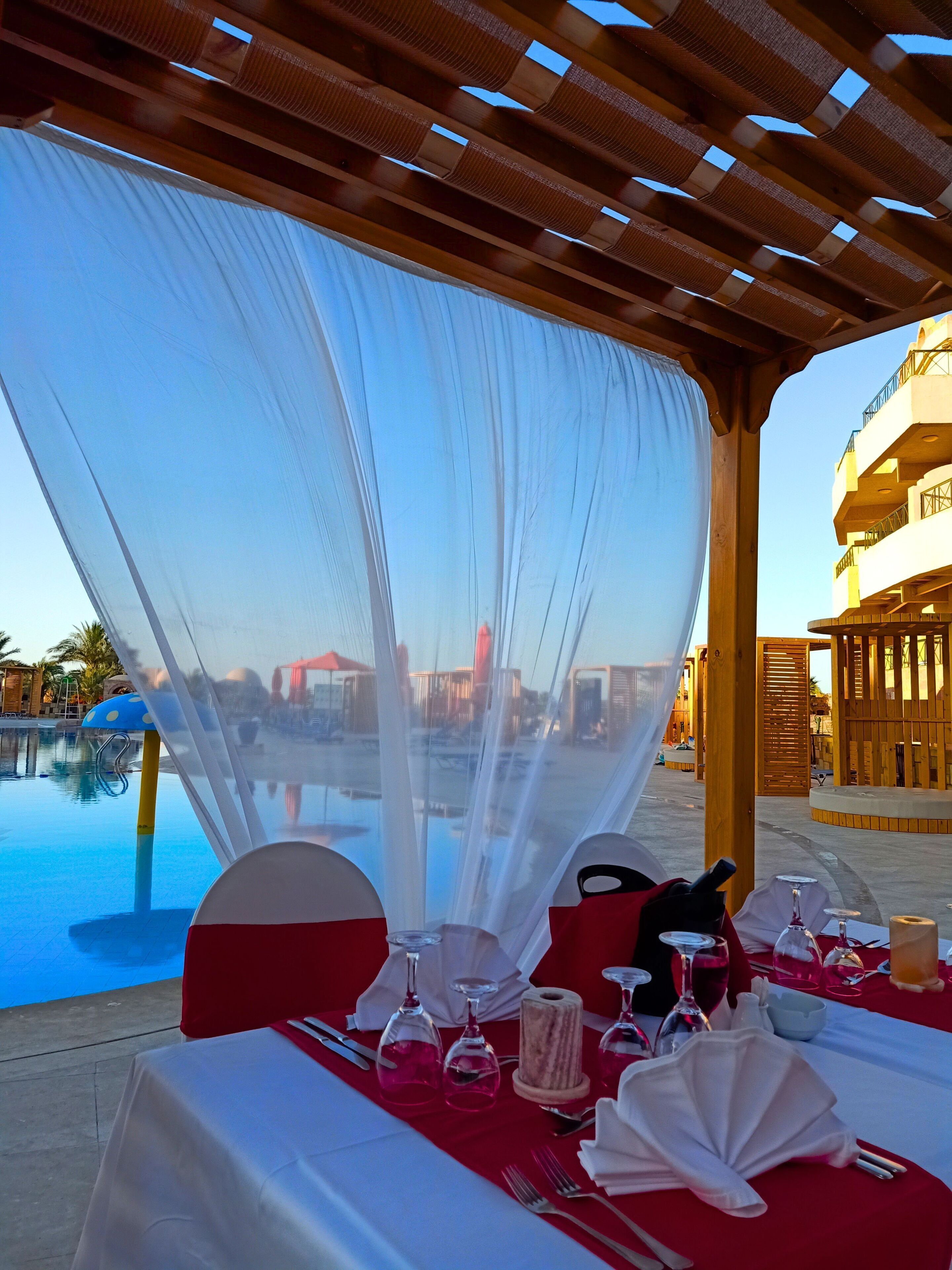 A table set for a meal with a view of a pool and a building in the background.