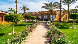 Un sendero bordeado de flores y palmeras que conduce a un edificio de piedra con arcos.