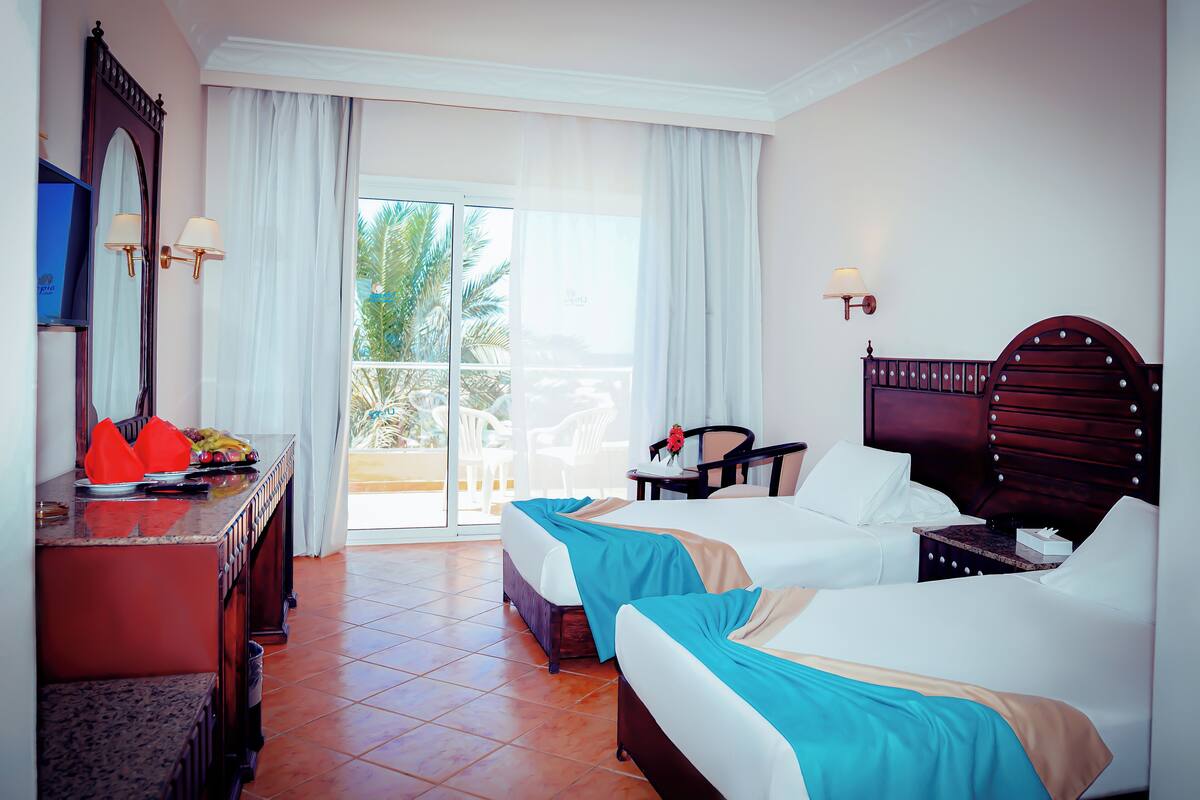A hotel room with two beds, a desk with a mirror, and a view of the outdoors.