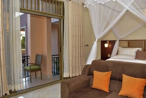 Habitación de hotel con cama, sofá, sillón y balcón con vistas.
