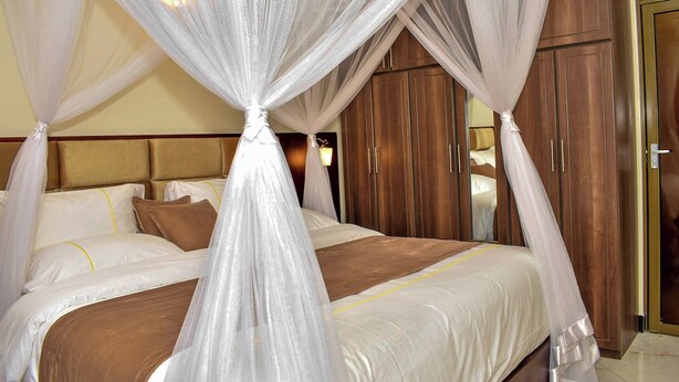 A bedroom with a four-poster bed, wooden wardrobe, and a mirror. - Studio Furnished Apartments Entebbe (Entebbe)
