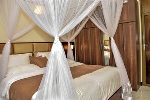 A bedroom with a bed covered by a canopy, wooden wardrobe, and a mirror.