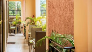 A corridor with wicker furniture and potted plants, leading to a balcony with a view of greenery. - Studio Furnished Apartments Entebbe (Entebbe)