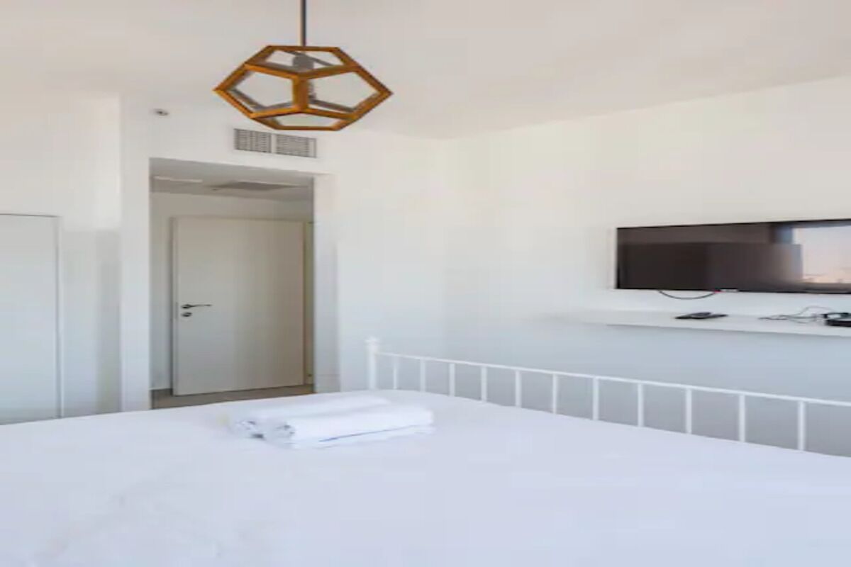 Una habitación de hotel moderna con una cama, un televisor montado en la pared y una puerta que da a otra estancia.