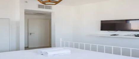 Una habitación de hotel moderna con una cama, un televisor montado en la pared y una puerta que da a otra estancia.