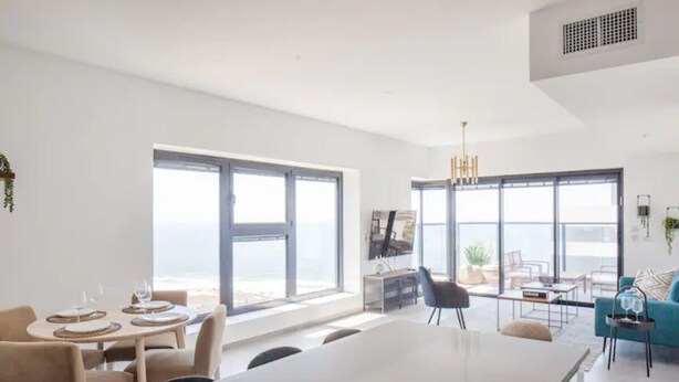 Una cocina moderna con ventanas amplias, un comedor con mesas redondas y una sala de estar con sofá y televisor.