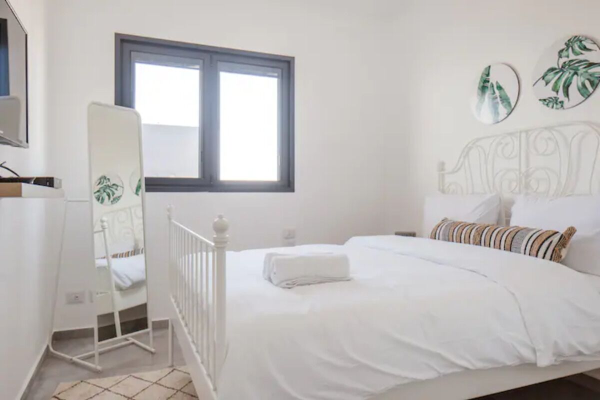 Een slaapkamer met een bed, een witte kapstok, een raam en decoratie aan de muur.