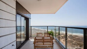 Un balcón con mesa y sillas de madera, una planta en maceta y vistas a la costa.