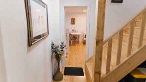 Un couloir doté d’un plancher en bois, un vase rempli de fleurs, un tableau encadré accroché au mur et un escalier avec des rampes en bois.