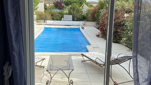 A view through a sliding glass door to a backyard with a swimming pool, two lounge chairs, and a table. - 100% self-contained studio at the foot of the Dentelles de Montmirail (Violes)