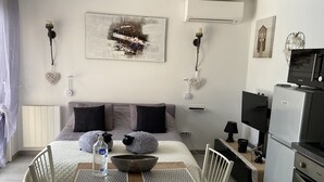 A modern, well-lit bedroom with a large bed, bedside tables, and a small kitchenette. - 100% self-contained studio at the foot of the Dentelles de Montmirail (Violes)