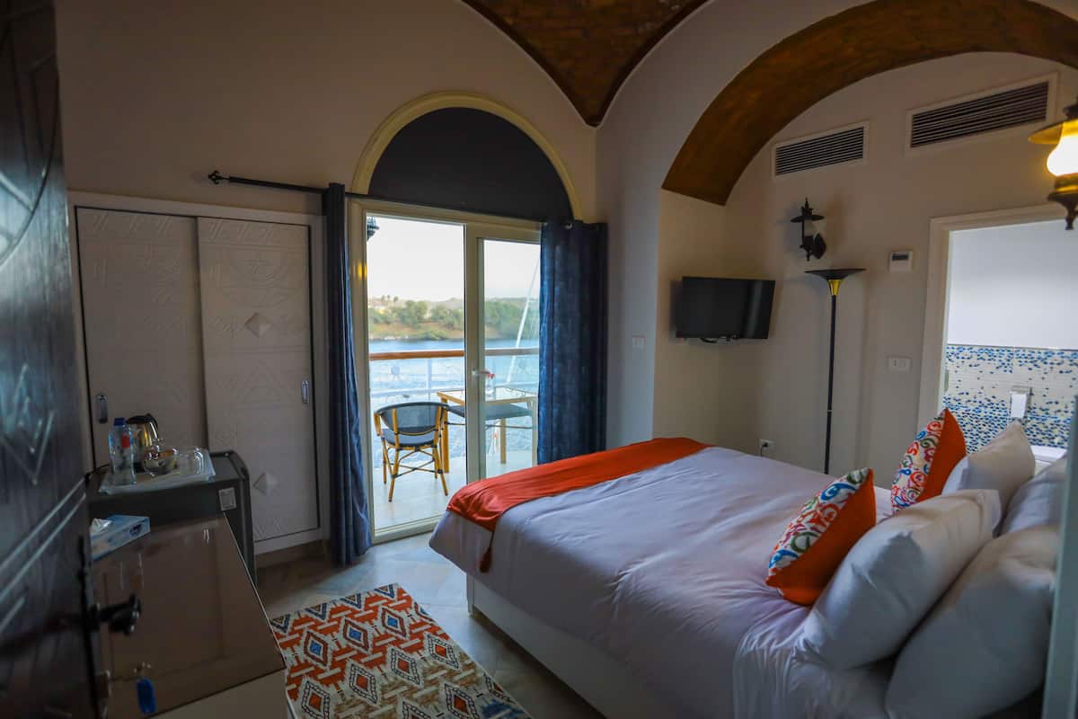 Habitación de hotel con cama, escritorio, silla, televisión y vista al mar a través de un ventanal.