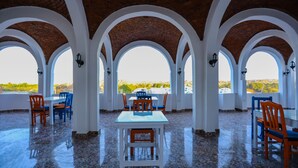 A covered dining area with a tiled floor, white tables and chairs, and arched ceilings. - NUB INN (Aswan)
