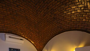 A bedroom with a brick ceiling, a white bed with orange and blue pillows, a white nightstand, and a white wardrobe. - NUB INN (Aswan)