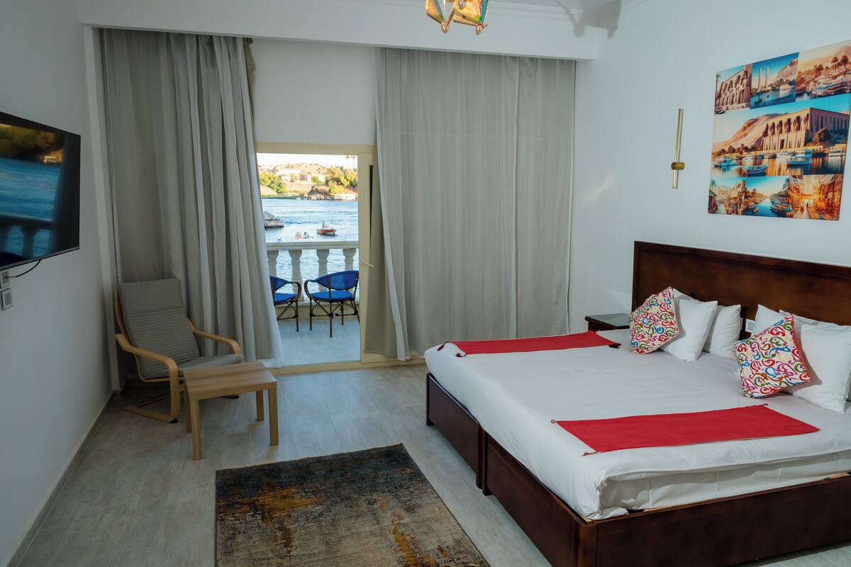 Habitación de hotel con cama, una silla, televisión, balcón con vista al mar y un cuadro en la pared.