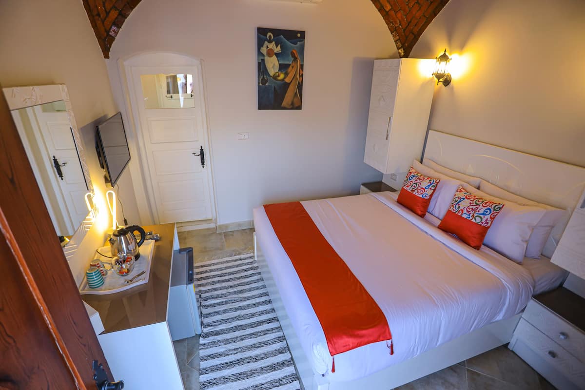 Un dormitorio con cama, mesitas de noche, escritorio, silla, espejo, cuadro y puerta.