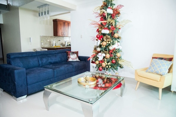 A living room with a blue sofa, a glass coffee table, and a Christmas tree.