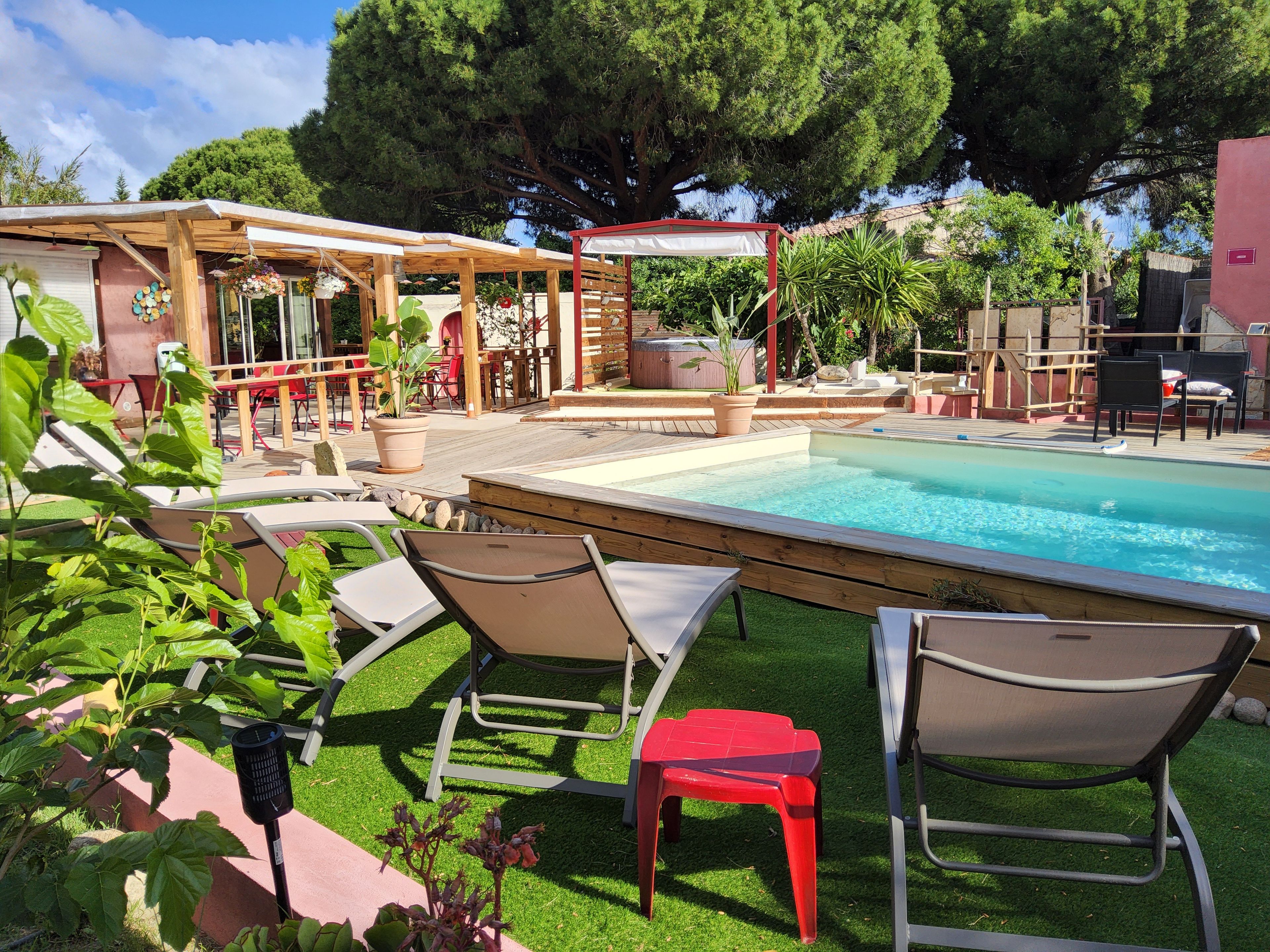 Un espace aménagé au bord de la piscine, avec des chaises longues, un jacuzzi et une pergola.